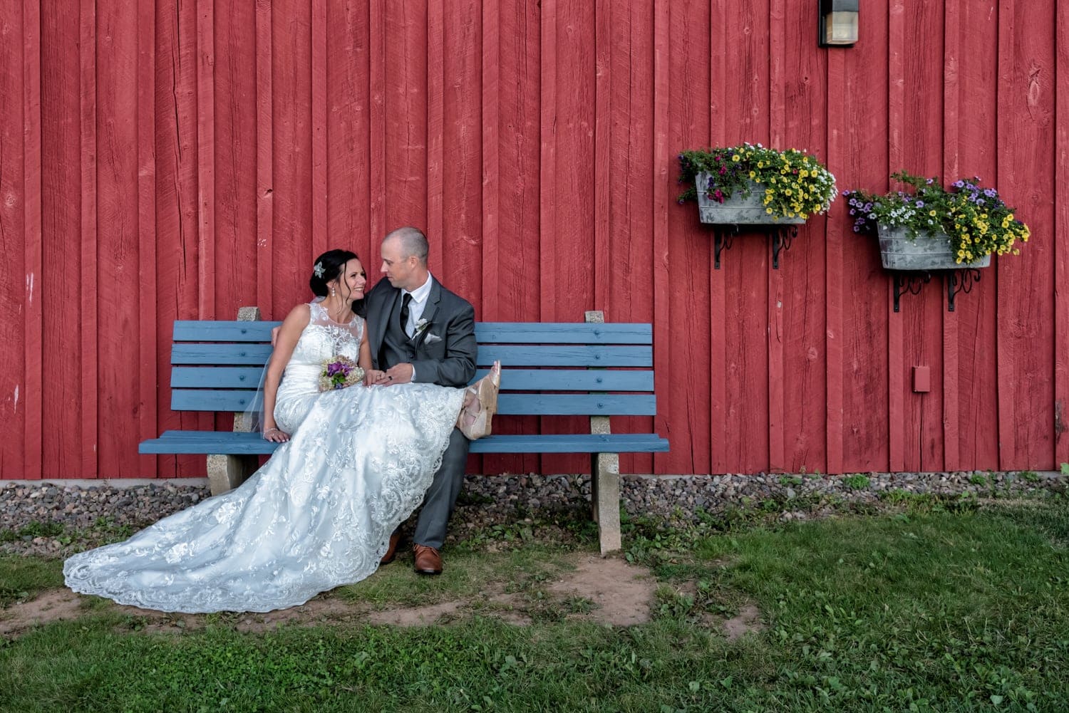 The bride and groom sitting on a wooden blue bench against the Heritage Barn at the Old Orchard Inn, Wolfville NS.