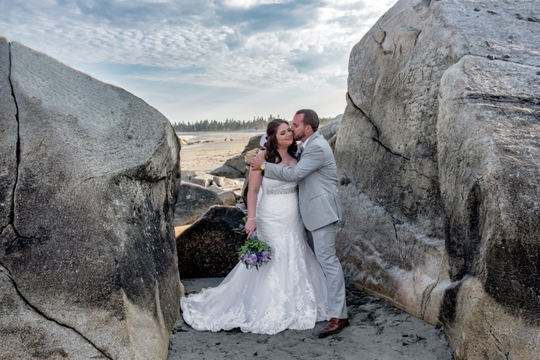 Candid bride and groom photos done on the beach between the rocks during a White Point wedding.