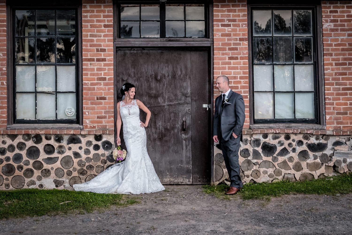The bride and groom wedding photos, they are standing against the wooden doors of an urban brick style building at the Old Orchard Inn.