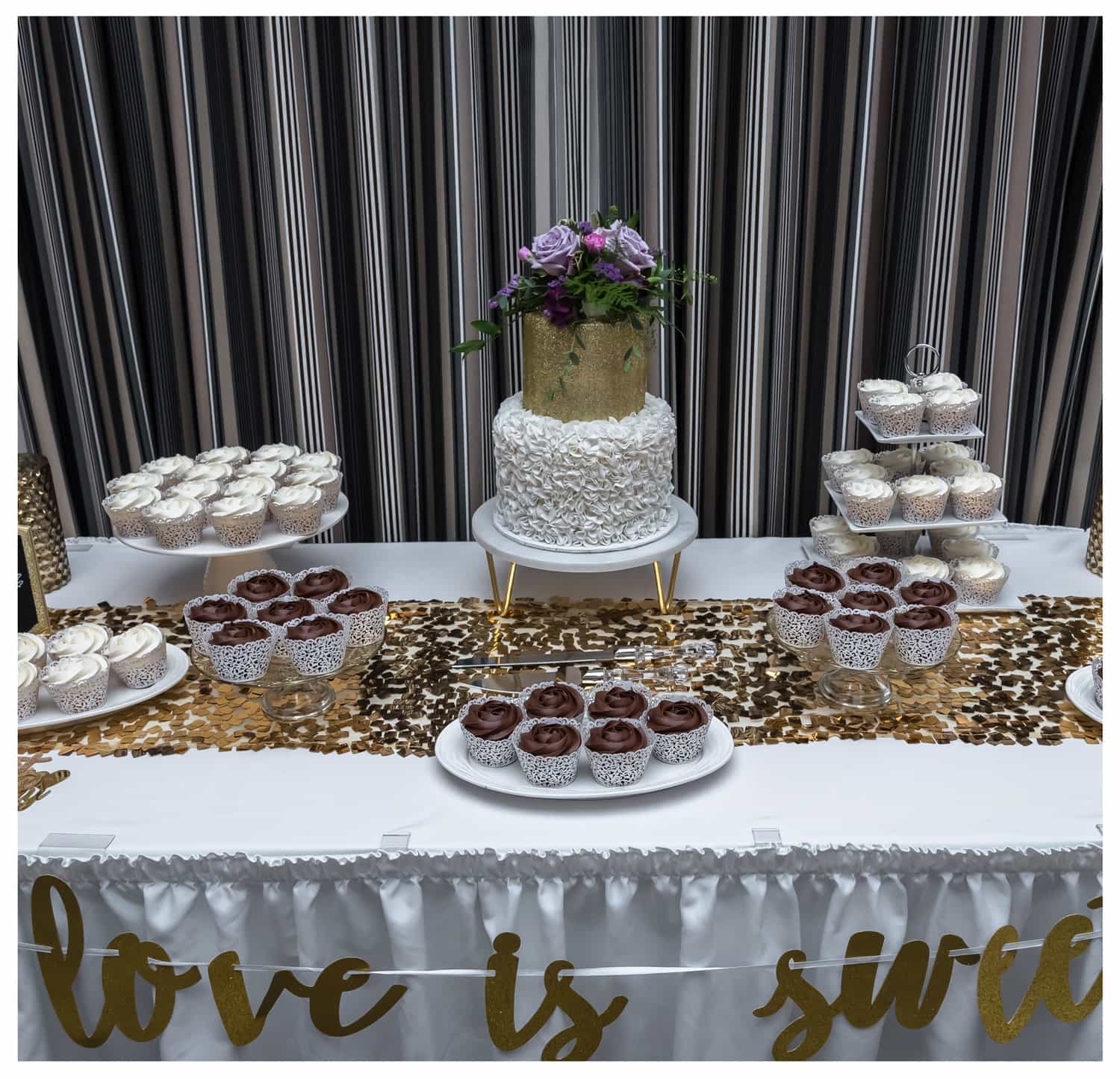 a two tier wedding cake with floral wedding cake topper surrounded by wedding cupcakes on three tier cupcake stands