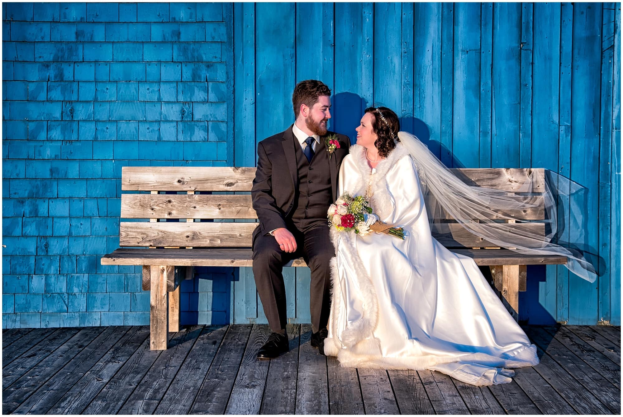 The bride and groom pose on a wooden bench for wedding photos at Fisherman's Cove in Eastern Passage, NS.