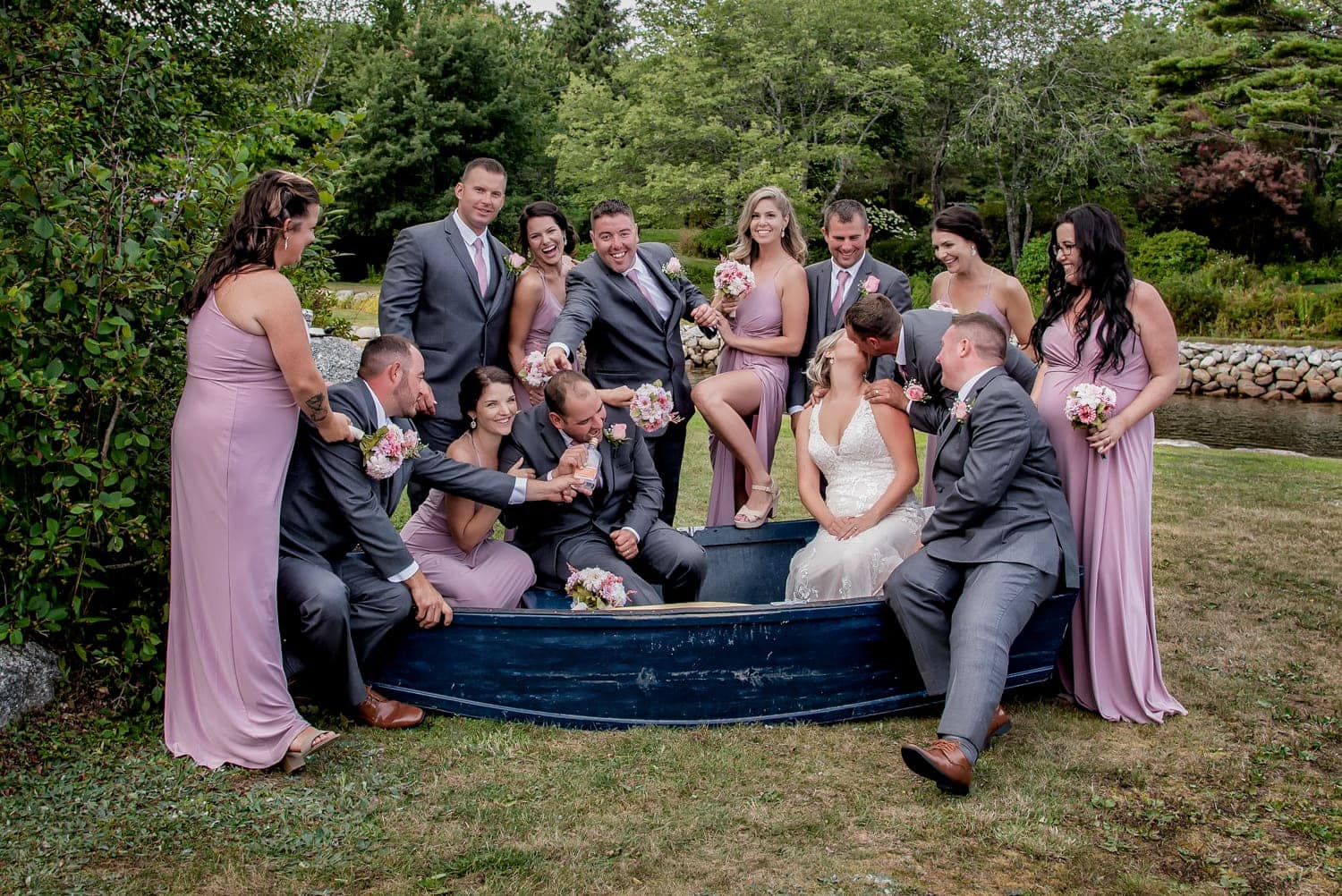 The bride and groom with the wedding party posing for wedding photos in a boat, bride kissing a groomsmen and groom drinking alcohol during a backyard wedding in Halifax.