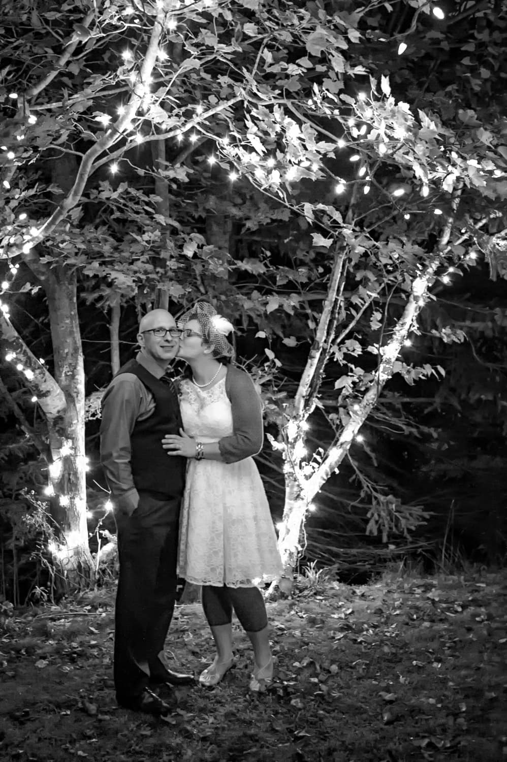 The bride kisses the groom infront of a tree of lit lightbulbs during their outdoor wedding in Cole Harbour NS