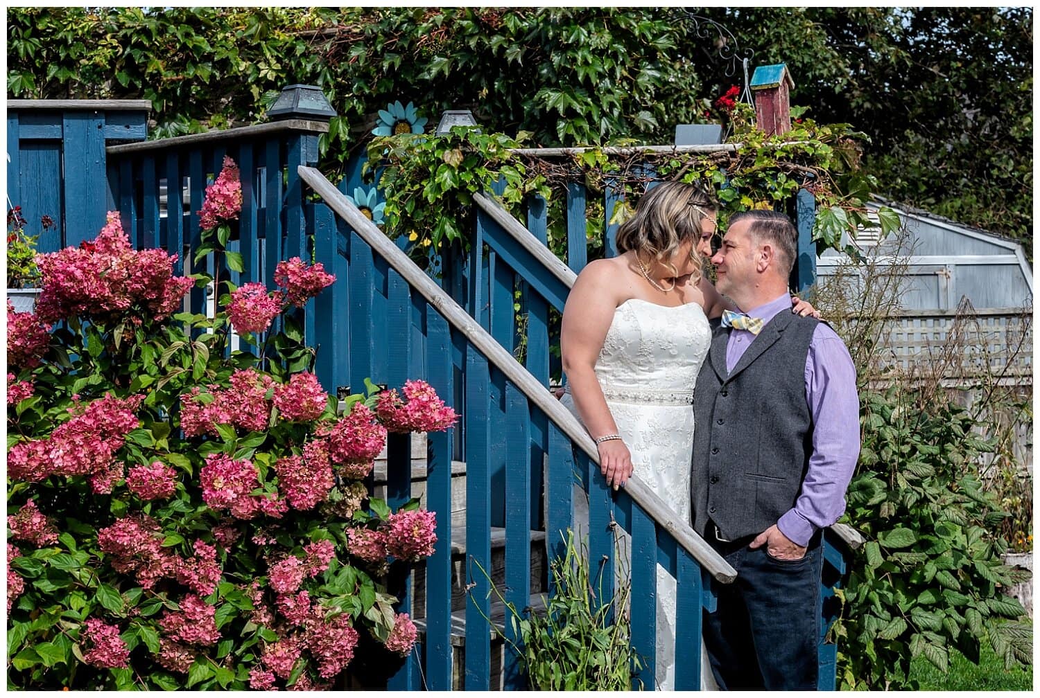 The bride and groom pose for wedding photos among the garden during their backyard wedding.