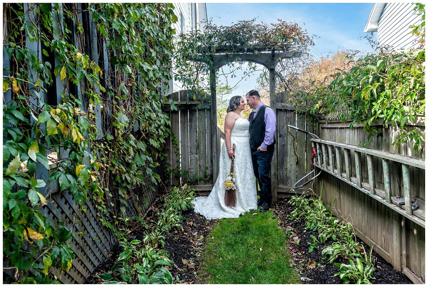 The bride and groom pose with the broom they jumped over during their wedding ceremony in a backyard wedding, Dartmouth NS.