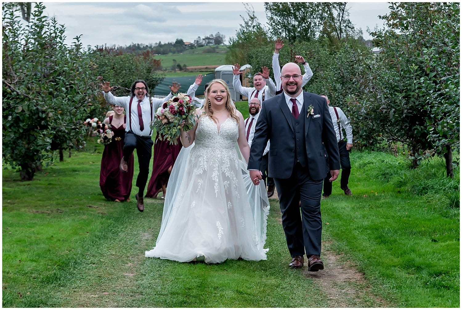 The bride and groom walk ahead as their wedding party jumps into the air behind them at the Bent Ridge Winery in NS.
