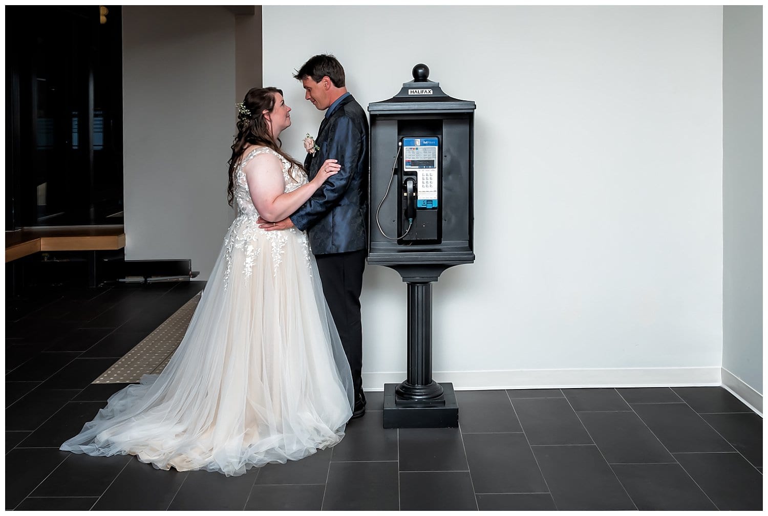 The bride and groom embrace near an old time phone booth at Alderney Gate in Dartmouth NS.