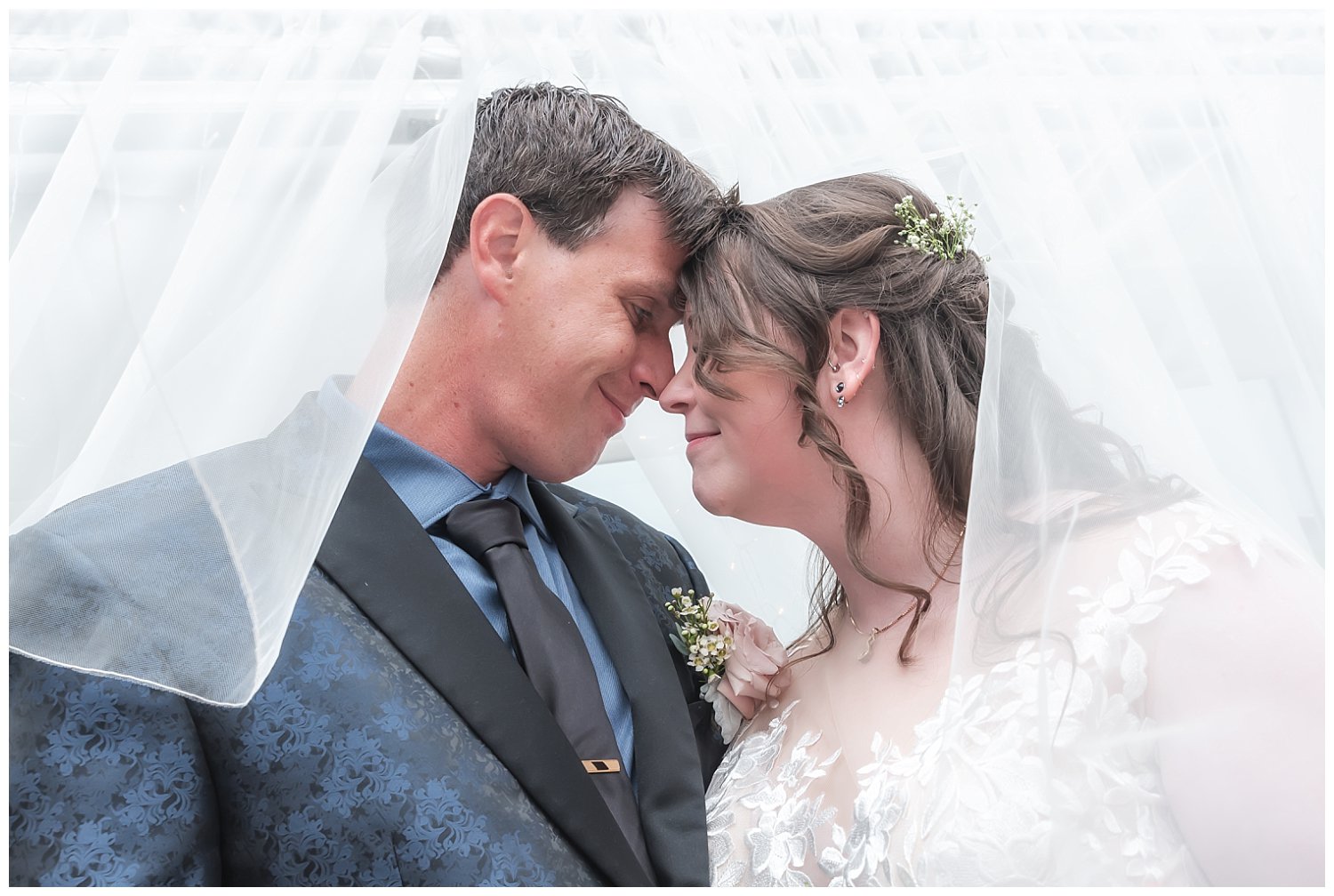 The bride and groom pose for wedding photos under her veil.