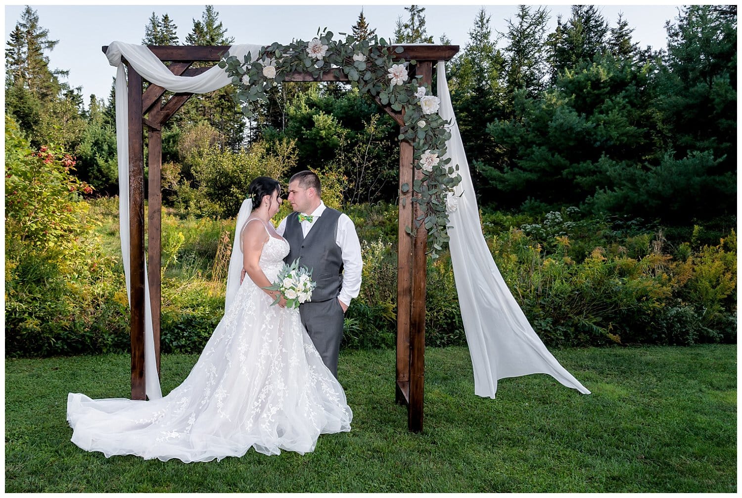 The bride and groom pose under a rustic trellis for wedding photos at the Hubbards Barn in NS.