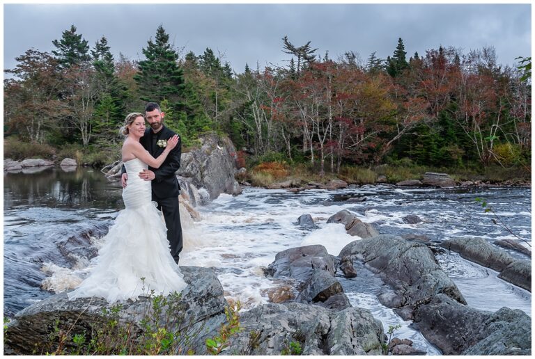 The bride and groom pose for wedding photos by a river and waterfall at Liscombe Lodge in NS.