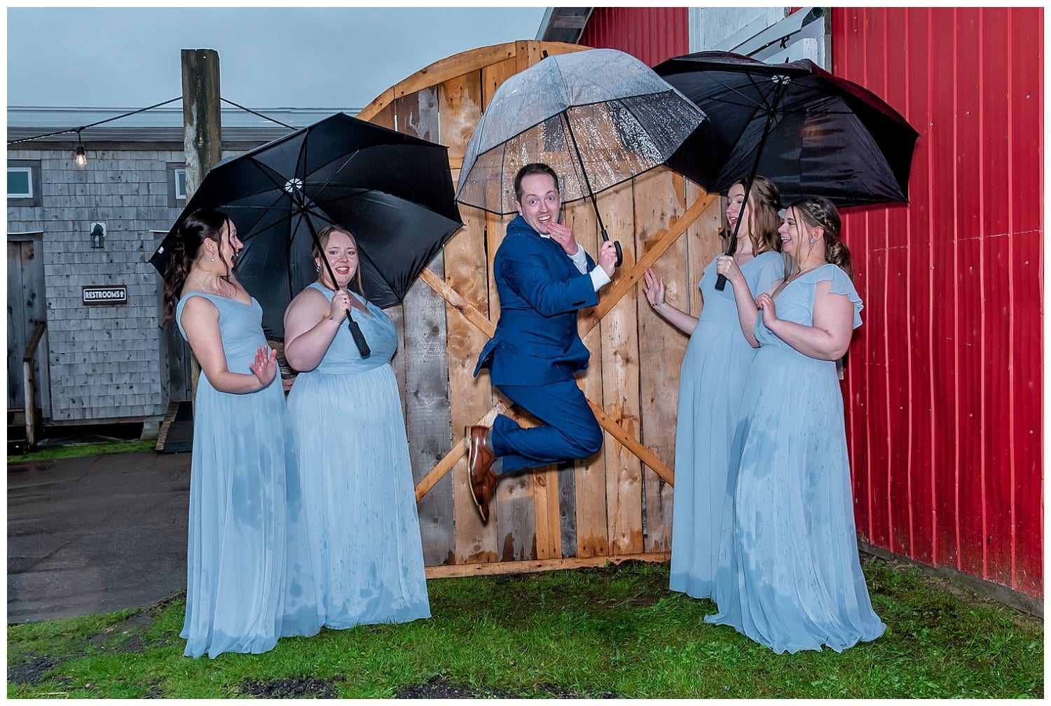 The groom posing for fun wedding photos with the bridesmaids at Parkers Barn in Hopewell NS.