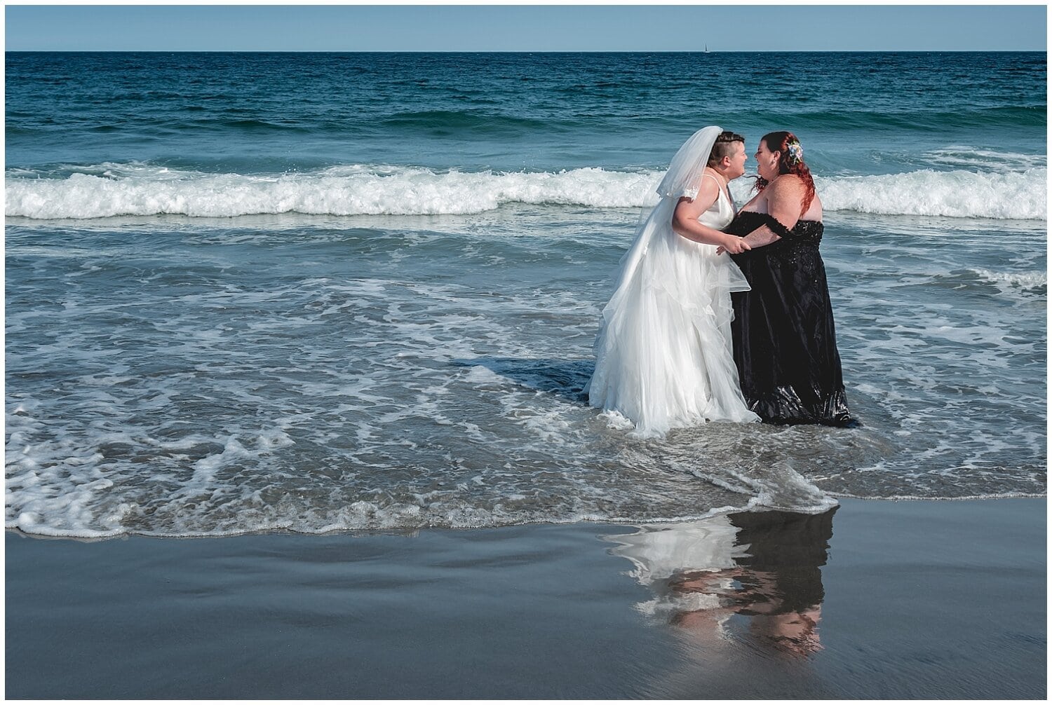 The brides take a dip in the ocean, laughing and having fun after their wedding ceremony at White Point Beach Resort in NS.