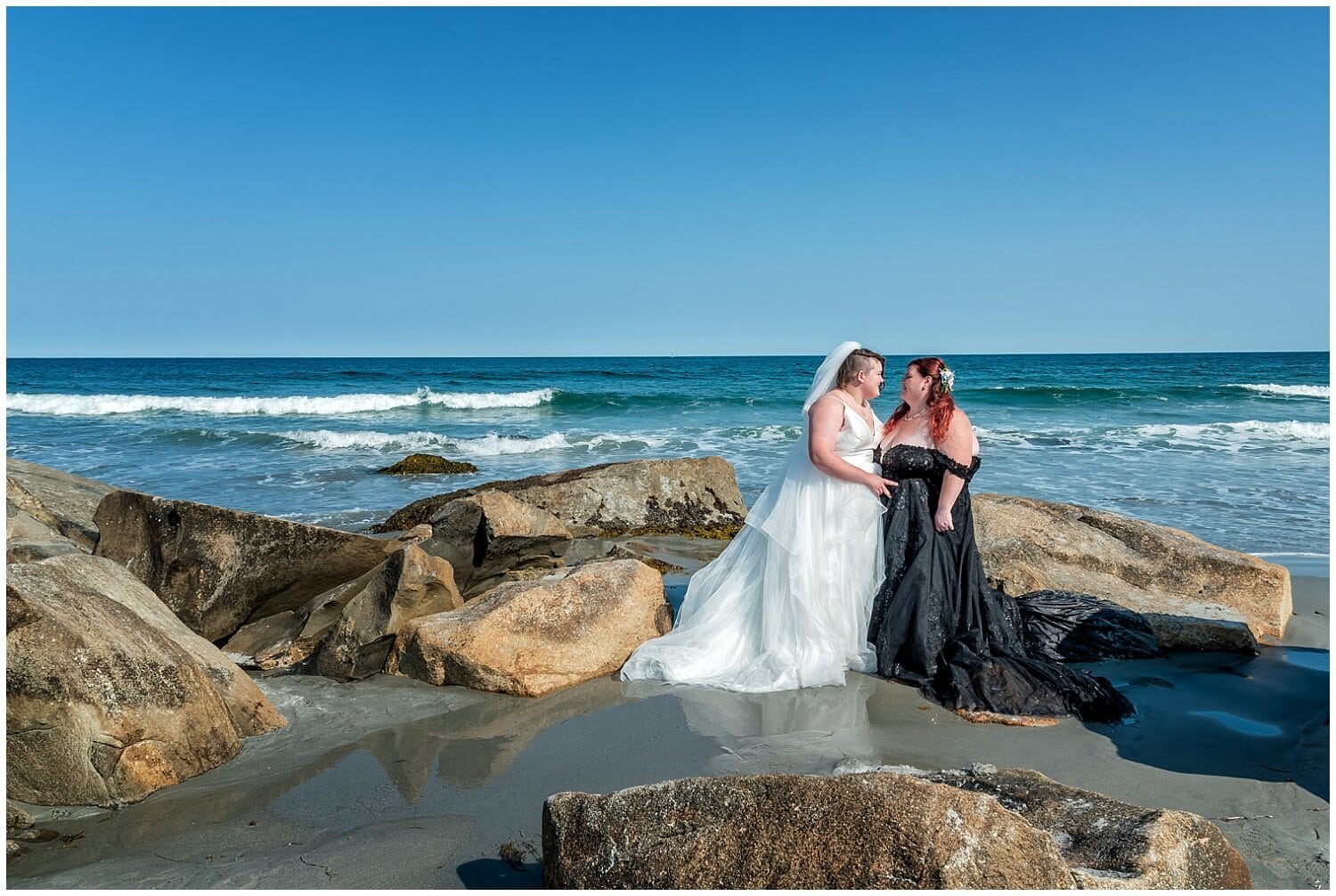 The brides pose for wedding photos at the ocean's edge after their wedding ceremony at White Point Resort in NS.
