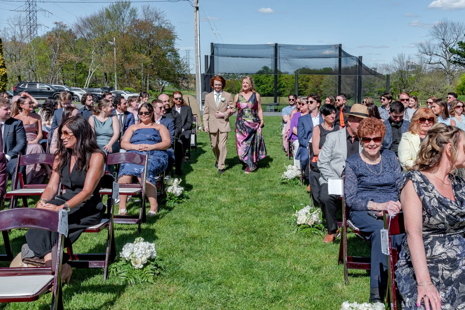 Groom walking down the aisle arm‑in‑arm with his mother during the outdoor ceremony at Ashburn Golf Club in Halifax.