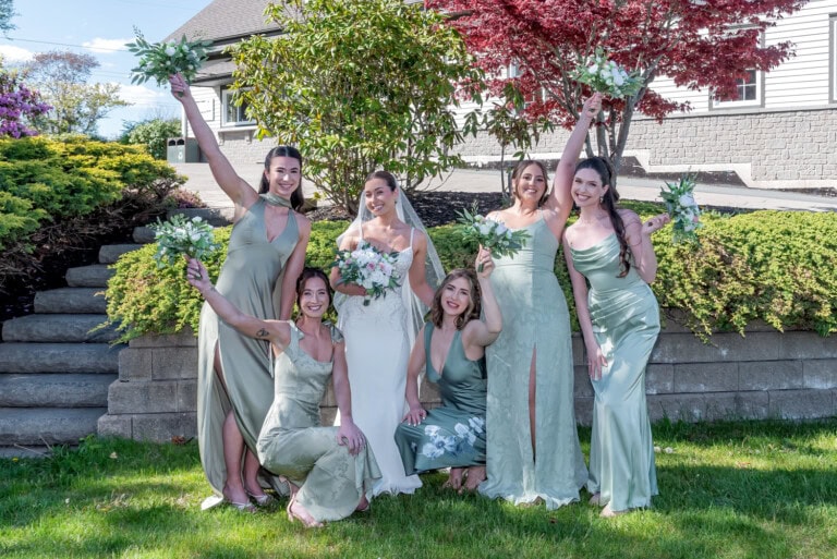 Bride and bridesmaids posing together outdoors at Ashburn Golf Club with bouquets raised in celebration in Halifax.