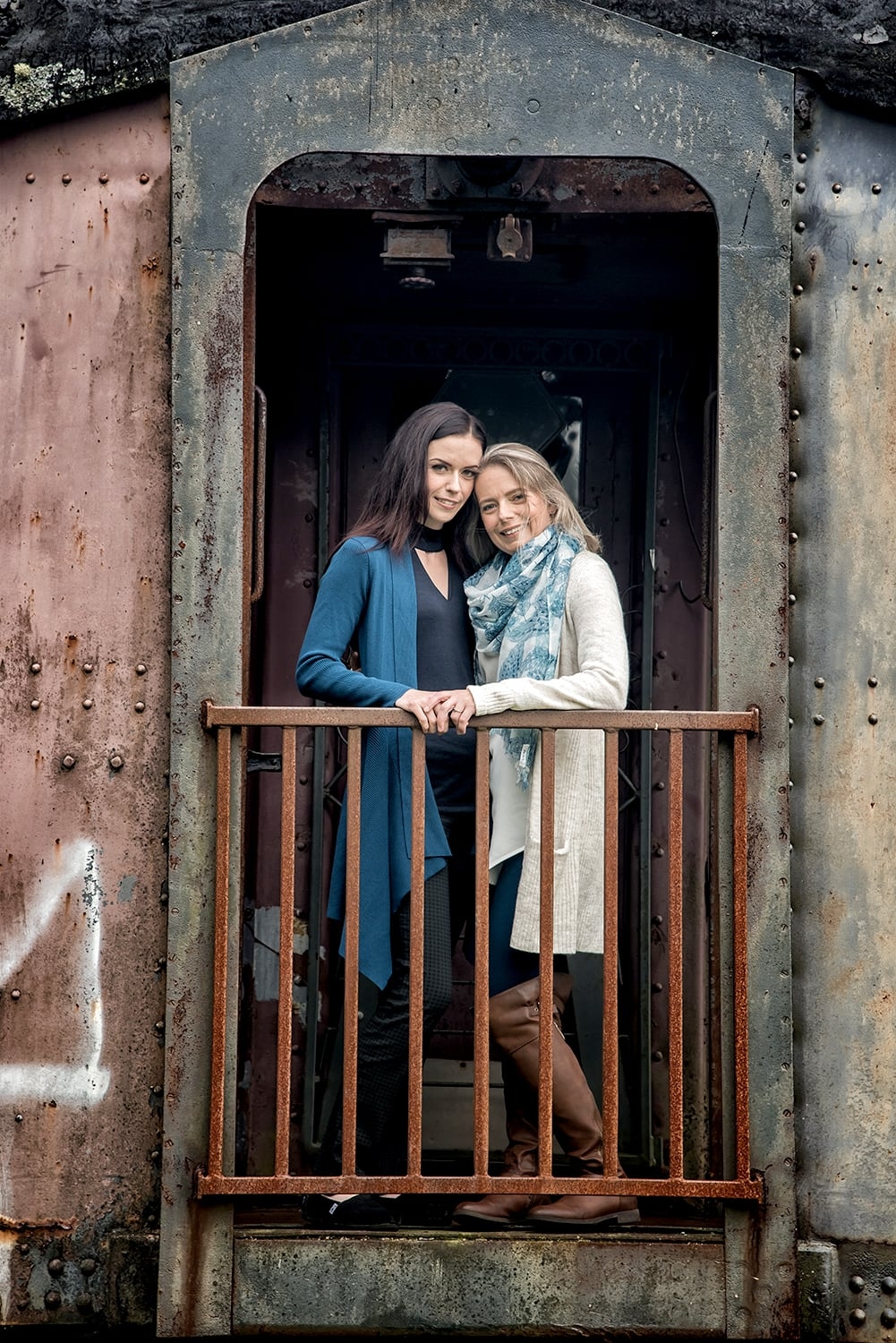 An LGBT lesbian couple stand on the deck of a train for engagement photos at the Musquodoboit Train Museum in Nova Scotia.