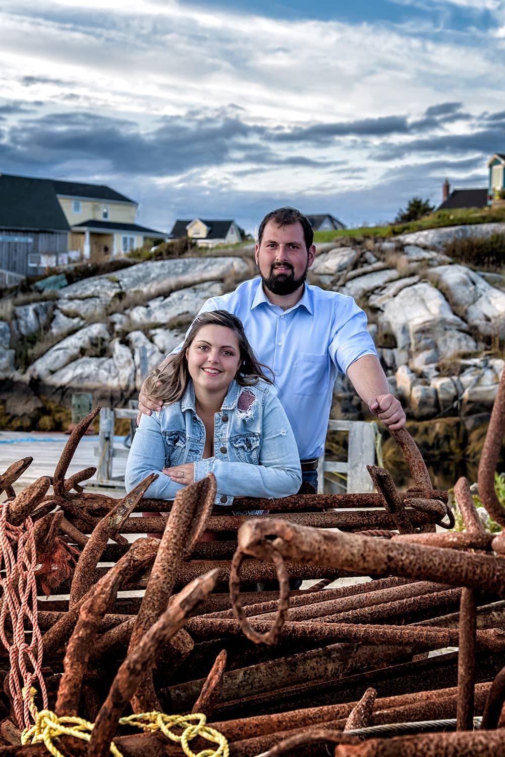 A newly engaged couple pose for engagement photos infront of rusty anchors at Peggys Cove Nova Scotia.