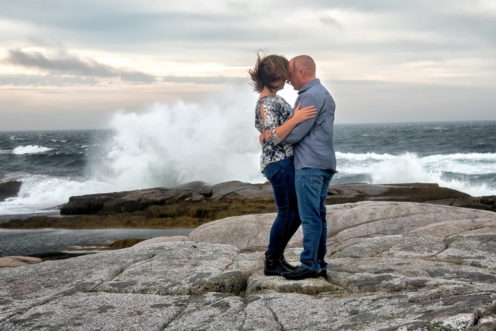 A cute couple embracing for their engagement photos at Peggys Cove in Nova Scotia.