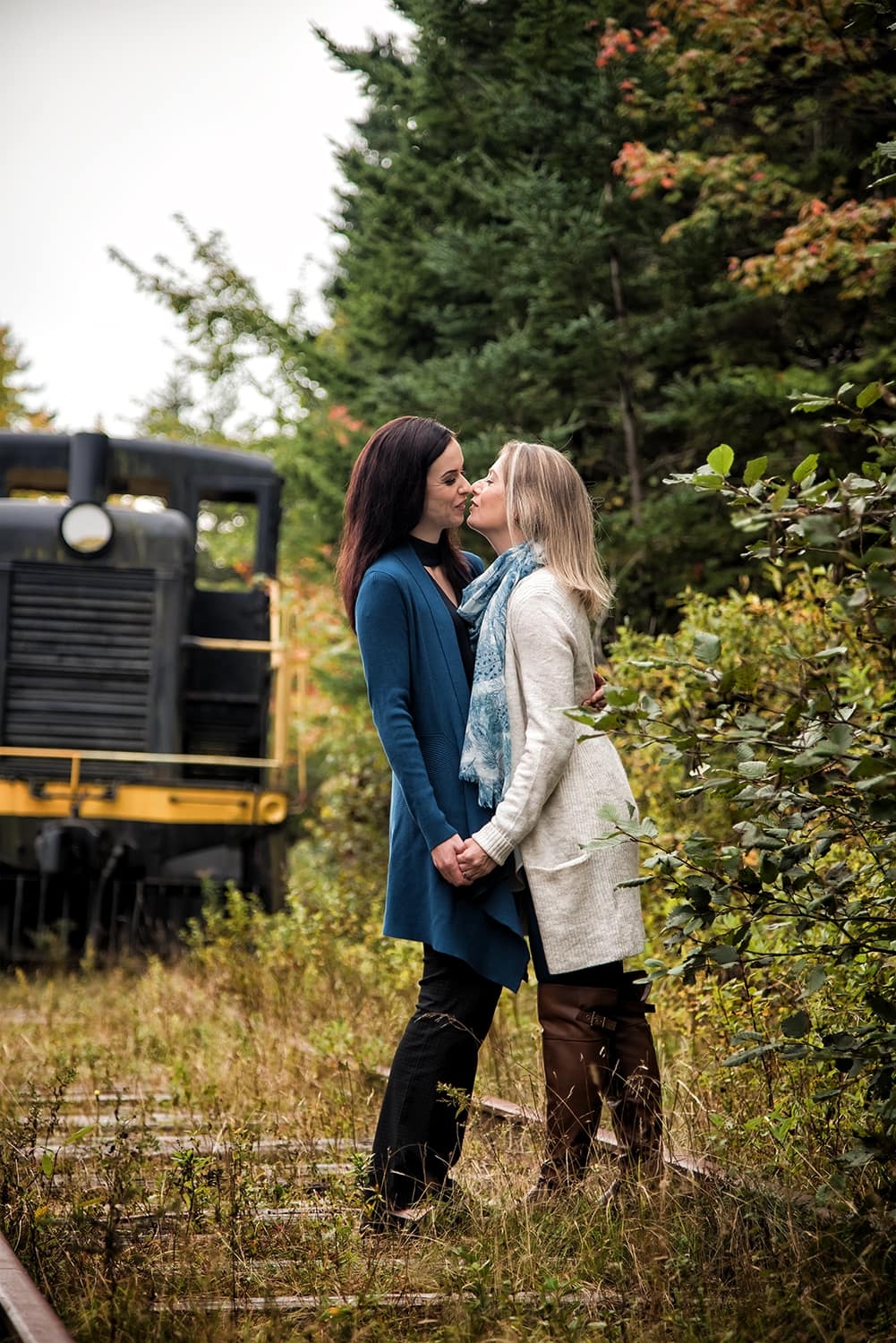An LGBT lesbian couple holding hands and kissing during engagement photos at the Musquodoboit Train Museum in Nova Scotia.