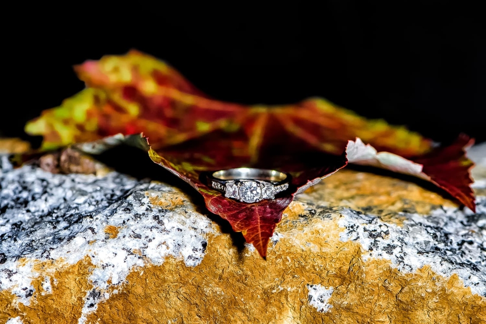 A custom designed engagement ring laying of an autumn leaf at Dingle Tower in Halifax NS.