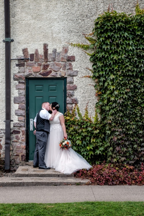 The bride and groom kiss against a stone and brick wall with veins, during their wedding photos at Digby Pines.