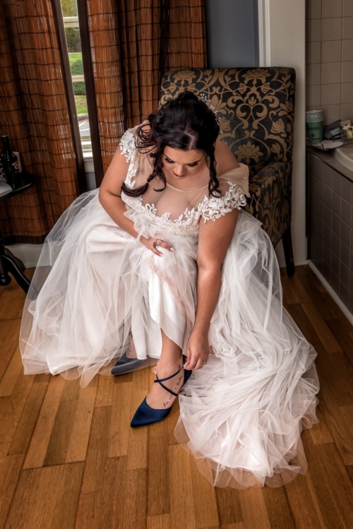 The bride in her wedding dress putting on her wedding shoes at Digby Pines.