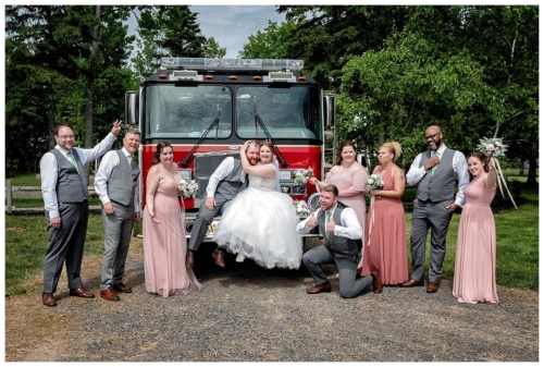 The wedding party have fun posing for wedding photos with the bride and groom on their fire truck at Healy Farm.