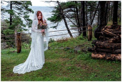 The bride poses infront of a rustic fence overlooking the Atlantic ocean for wedding photos in Bear Cove NS.
