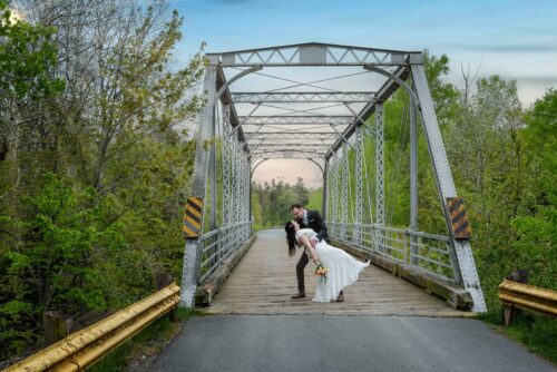 The Groom dips the bride infront of a bridge on their wedding day at Laurie Park in Nova Scotia.